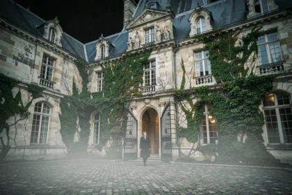 Façade gothique d'un manoir hanté parisien la nuit avec brume et grille en fer forgé, une femme en manteau sombre à l'entrée
